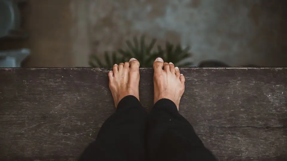 Close-up view of bare feet peeking over a wooden plank, creating a sense of vertigo and adventure.