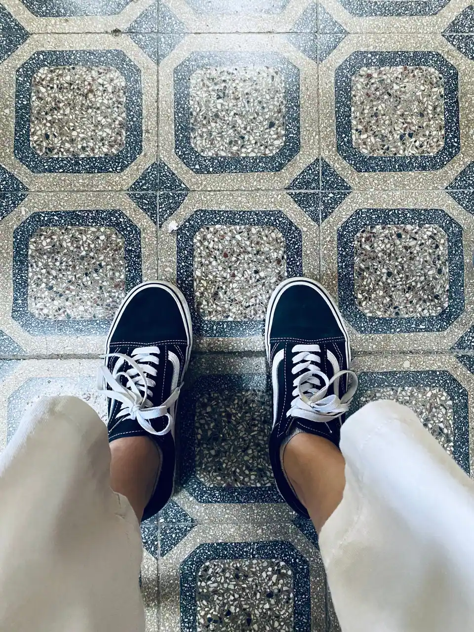 Black and white sneakers viewed from above on a stylish tiled floor.