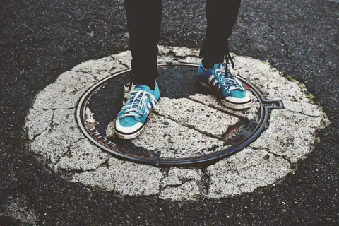 Blue sneakers standing on a weathered manhole cover in a city street.