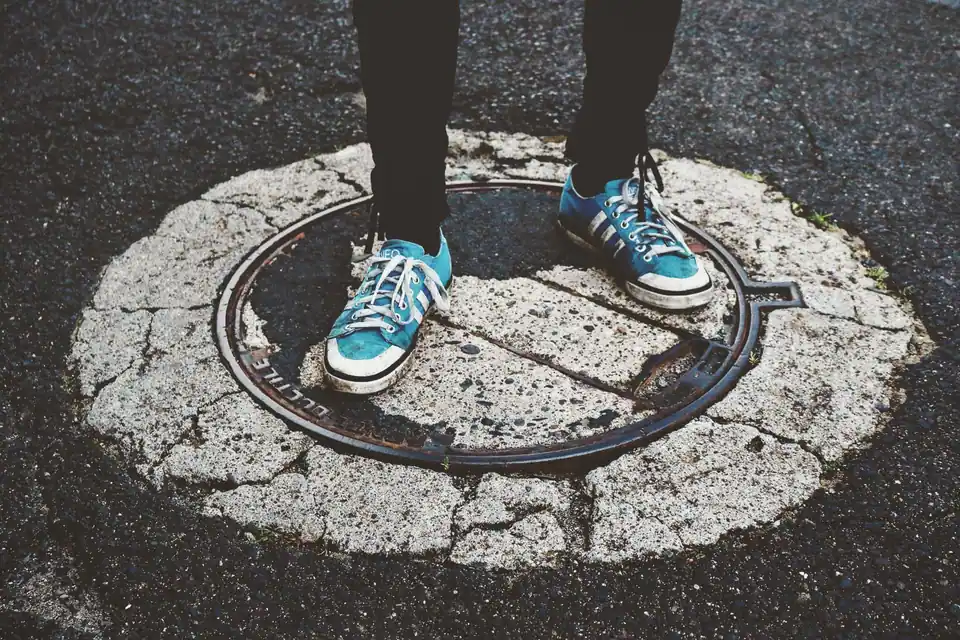 Blue sneakers standing on a weathered manhole cover in a city street.