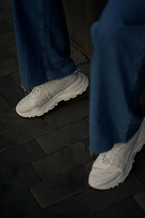 Close-up of stylish white sneakers paired with denim jeans on an urban street.