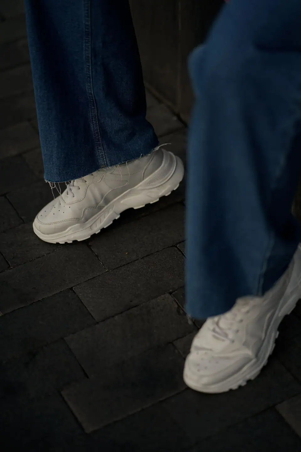 Close-up of stylish white sneakers paired with denim jeans on an urban street.