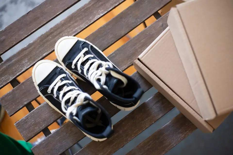 Black high-top canvas sneakers on a wooden bench beside cardboard boxes