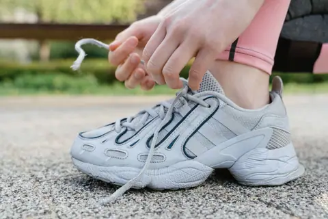 Close-up of a woman tying shoelaces on white sneakers during an outdoor exercise session.