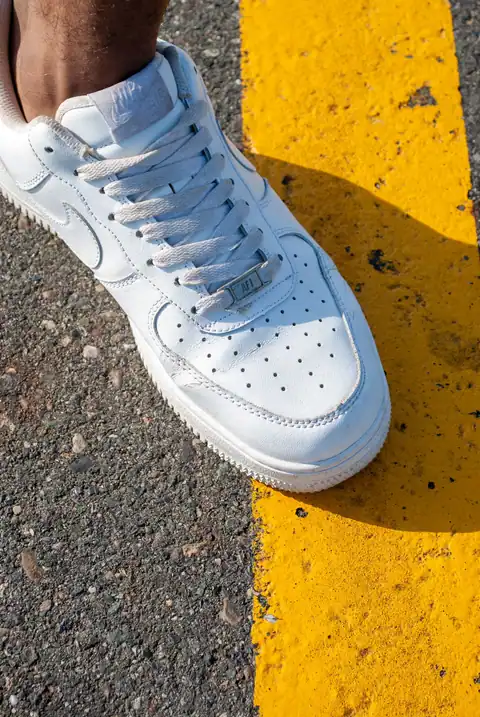 Close-up of a white sneaker stepping on a yellow line on an asphalt road.