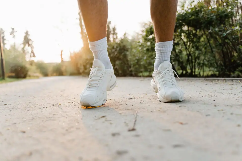 Close-up of legs wearing white sneakers walking on a sunlit path outdoors.